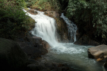 A serene waterfall flowing over rocks, surrounded by lush green vegetation. © k33pcalmncapture