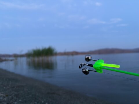 Fishing rod tip with green bite alarm bells by a lake at dusk