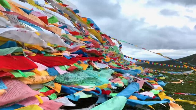 Tibetan prayer flags blowing in wind on grassy hillside under overcast sky