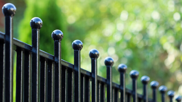 Black metal fence with ball finials providing security and boundary for a garden or property in sunlight