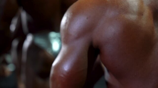 Muscular bodybuilder flexes oiled tanned arm bicep in dramatic studio lighting, showcasing fitness dedication, athletic definition, and intense physique power. 4K video.