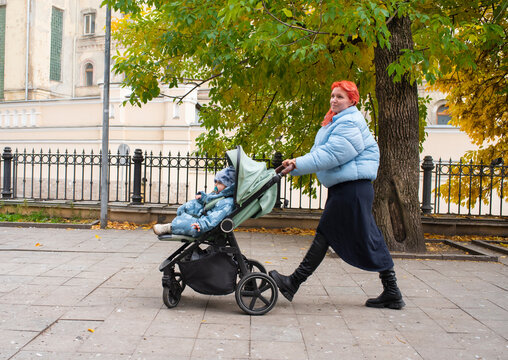 Mid adult 44 years old woman walking with sleeping baby in stroller on city street