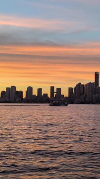 Evening in Toronto with a beautiful colorful sky downtown skyline and a calm lake with a small boats water taxi crossing it - view from the island. Vertical, general view Toronto, Ontario, Canada 