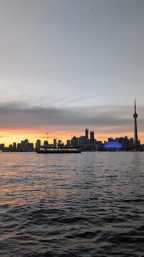 Evening in Toronto with a beautiful colorful sky downtown skyline and a calm lake with a ferry crossing it - view from the island. Vertical, general view Toronto, Ontario, Canada 