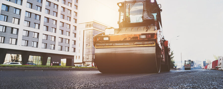 Daytime Urban Street Paving as a Large Roller Compacts New Asphalt Concrete
