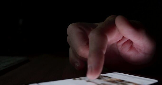 Hand interacting with a smartphone touchscreen in a dark environment. Concept of late-night digital browsing, social media addiction, screen glow, and mobile connectivity. 4K.