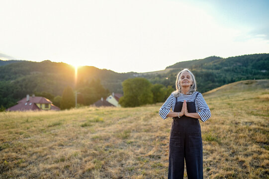 Senior woman practicing meditation outdoors in peaceful countryside.