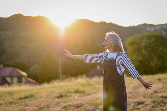 Senior woman practicing meditation outdoors in peaceful countryside.