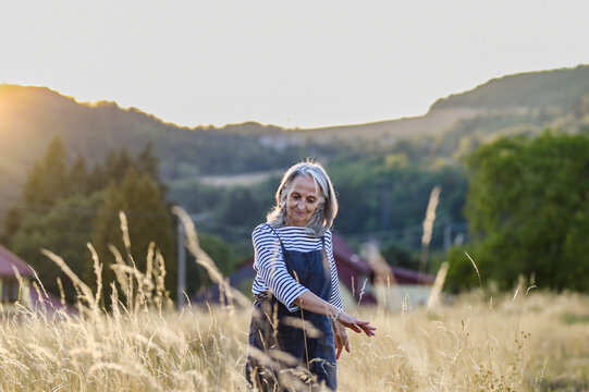 Active older woman enjoying peaceful walk through countryside in golden sunlight.