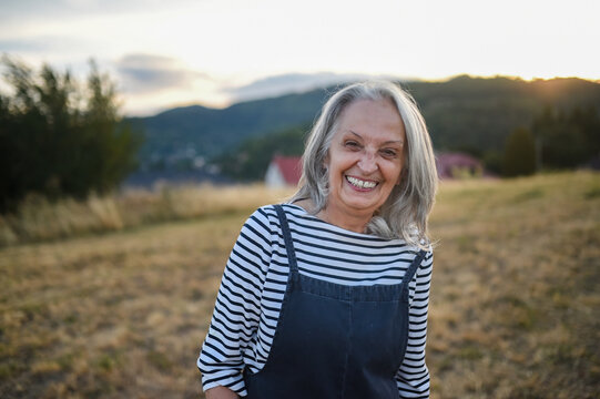 Active older woman enjoying peaceful walk through countryside in golden sunlight.