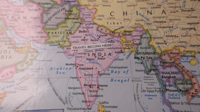 Hand revealing Travel Begins Here sticker on world map pointing at India