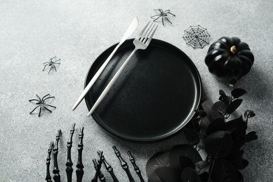 Black Halloween table setting with plate, cutlery, pumpkin, and spider decorations on a textured background