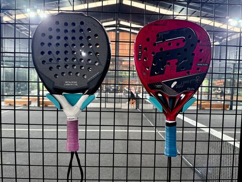 Depok, Indonesia - October 3, 2026: Close-up view of a modern adidas pala padel racket hanging on the wire fence of an indoor court. The background shows a blurred view of the turf playing surface