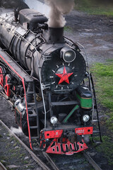Steam locomotives from USSR with red star stands and smoke from the steam locomotive's chimney on the railroad tracks in the museum exposition. Retro steam train. © VLAD ANTONOV