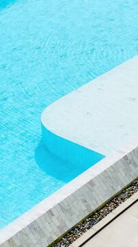  Vertical view of clear blue water and white tile edge of luxury swimming pool at modern resort.
