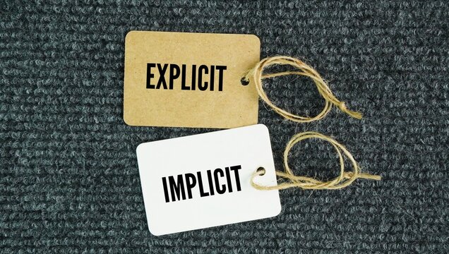 Paper tag with the words explicit and implicit. Explicit means stated clearly and directly, while implicit means hinted or implied without being plainly expressed