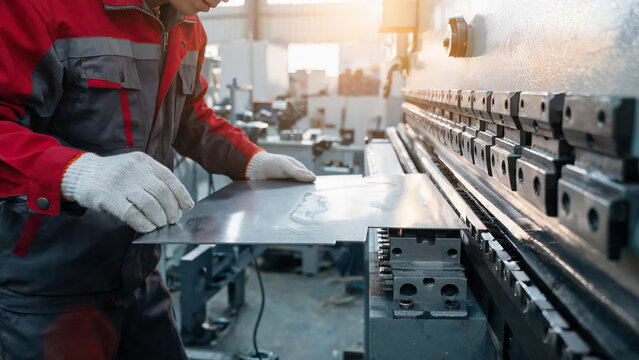 A factory worker positions a metal sheet on a bending machine for industrial metalworking and fabrication tasks.