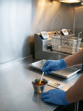 Checking Deep Fryer Oil Quality with Test Strip in Kitchen