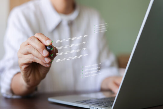 Business person holding stylus pen checking off virtual checklist boxes with laptop. Concept of quality control, task completion, online survey, compliance standard, and performance evaluation.