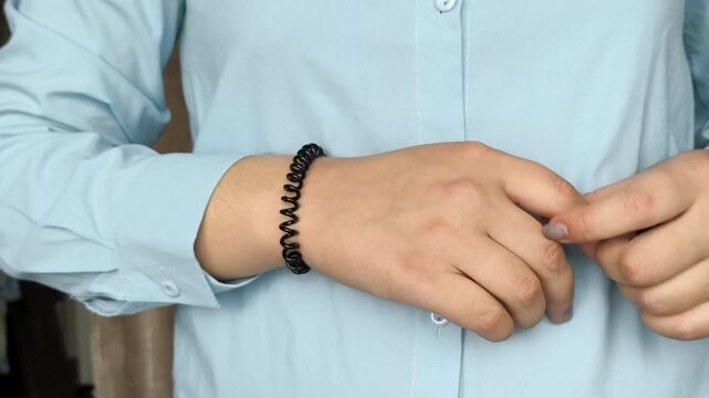 a woman wearing a black spiral hair elastic on her wrist, representing a convenient hair accessory and casual fashion detail.