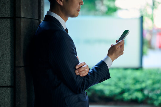壁にもたれてスマートフォンを見る男性ビジネスマン