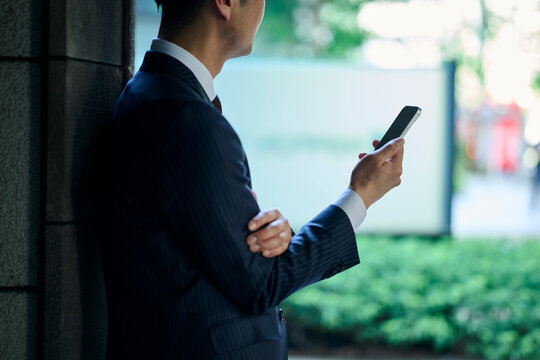 壁にもたれてスマートフォンを見る男性ビジネスマン
