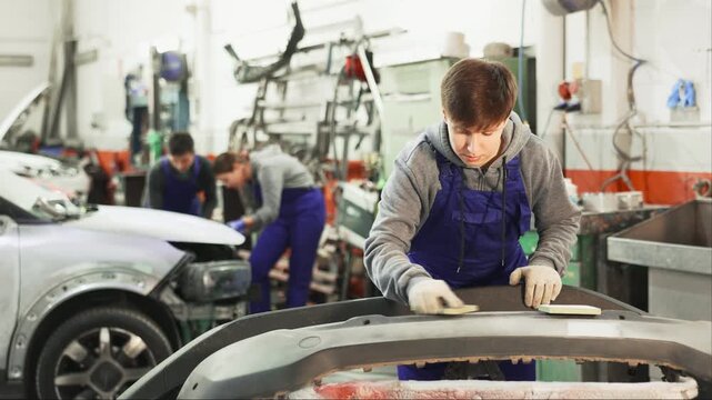 Guy worker removes dents on cars exterior, restores vehicle to its original form. Male auto mechanic polishes bumper, eliminating deformations, hiding flaws. Business hour 24 service coverage. 