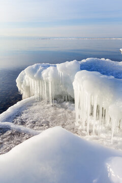 Ice-covered shore of Lake Baikal on cold quiet December day. View of coastline featuring white ice floes and icicles during freeze-up period. Scenic waterscape. Changing of seasons. Natural background