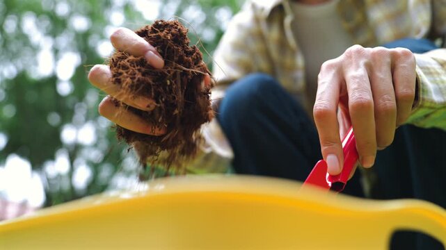 Woman hands using red shovel to mix potting soil, peat moss, and perlite in bin outdoor. Plant care, agriculture, and eco-friendly hobby concept.