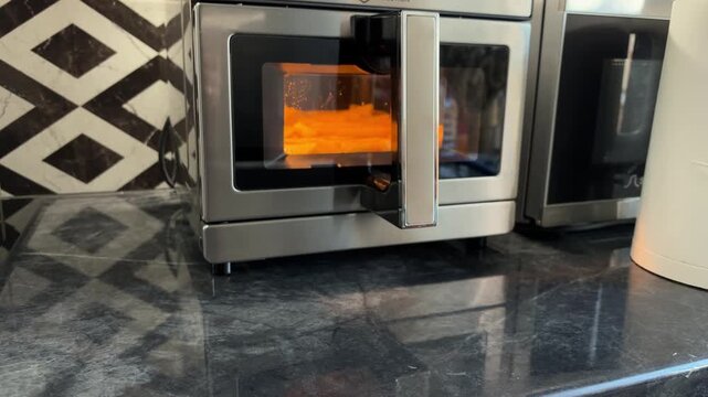 A compact oven cooks potato sticks on a kitchen counter with a tiled backsplash, home cooking, household appliance, meal preparation.