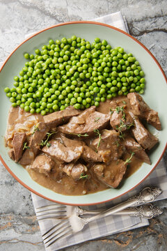 German baden beef liver with onions, braised in white wine and served with green peas close-up shot on a plate on a table. Vertical top view from above