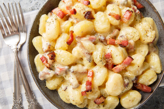 Close-up of potato gnocchi with fried bacon, velvet sauce, and Parmesan in a bowl on a table. Horizontal top view from above