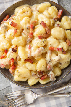 Italian gnocchi carbonara coated in a velvety egg yolk, pancetta and Parmigiano sauce closeup on the plate on the table. Vertical top view from above