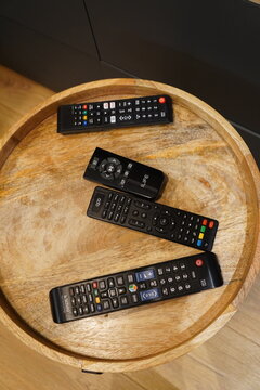 Collection of various black electronic remote controls resting on a round wooden coffee table