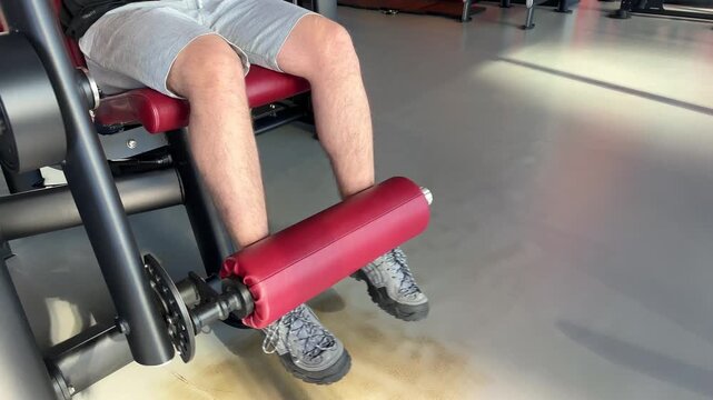 A man extends his legs on a gym machine with another adult behind him, quadriceps workout, resistance training, active lifestyle.