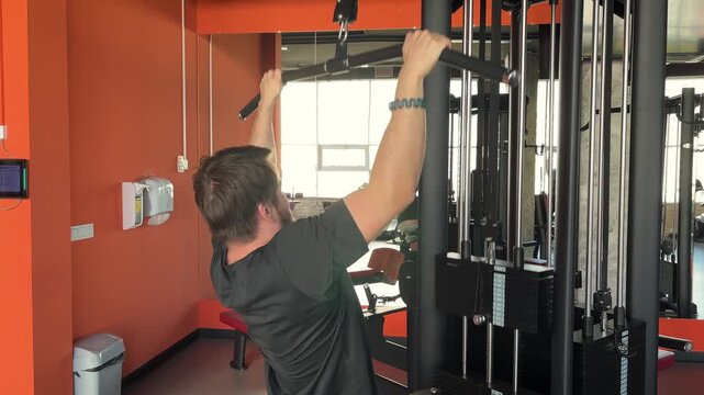 A man performs lat pulldowns while another adult appears in a gym mirror, back training, strength workout, active lifestyle.