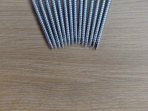 Sharp tips of metallic wood screws lined up on wooden surface