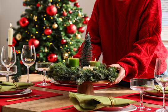 Christmas dinner preparation, person in red sweater setting festive table with candles and evergreen wreath for holiday celebration and family gathering
