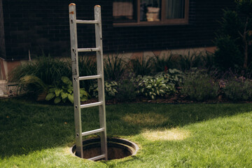 Fototapeta premium Aluminum ladder entering open manhole on green lawn