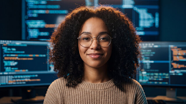 Smiling young woman with dark curly hair wearing round glasses and beige knitted sweater
