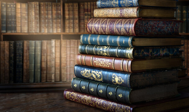 Stack of antique books with richly decorated leather bindings, gilt tooling, raised bands and ornate embossed spines, displayed against a warm old library background. 