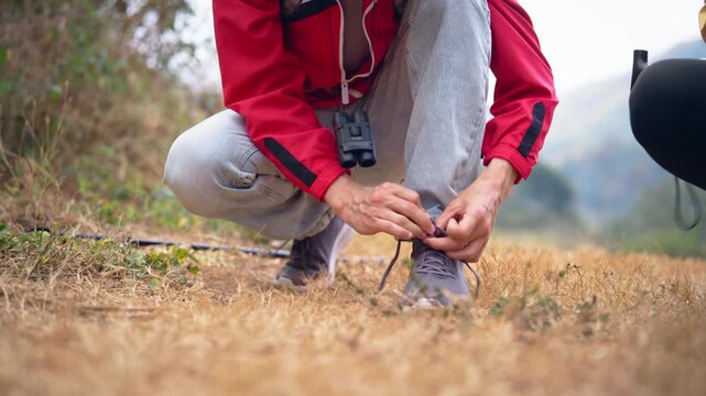 Close up of male hiker with backpack tying his shoes on mountain trail. 