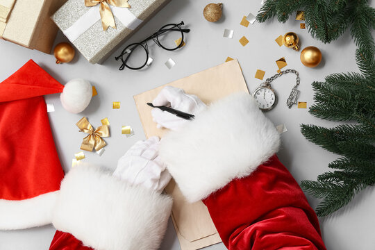 Santa Claus with Christmas decorations, gift boxes and pocket watch writing letter on grey background
