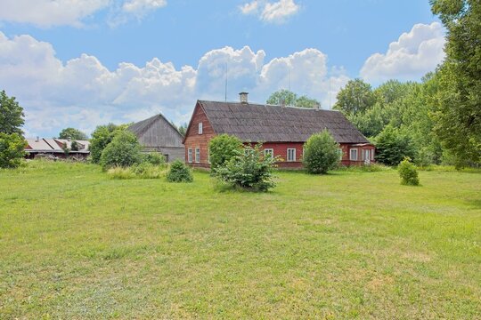 Old, traditional Baltic wooden farmhouse painted in a rustic red color. It features a long, weathered gabled roof, classic white-trimmed window frames, and a stone foundation, Estonia, Europe.