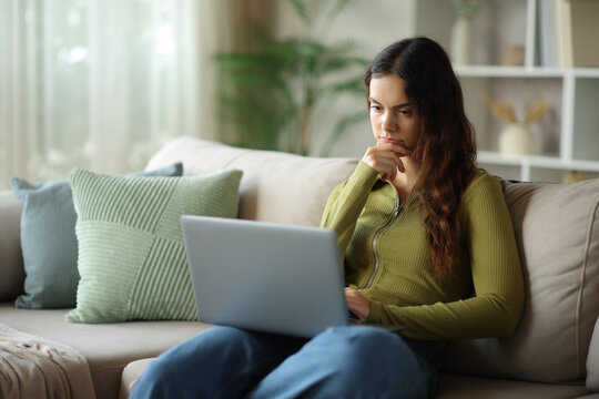 Pensive young woman checking laptop at home