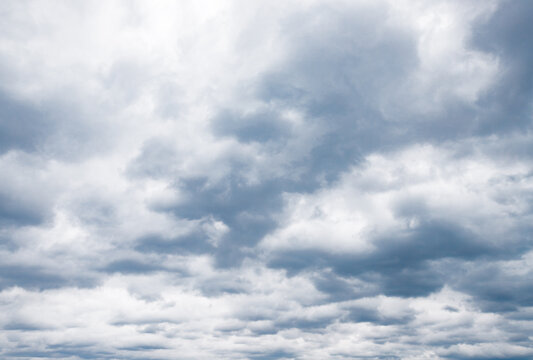 Stratocumulus clouds fill an overcast sky, dense gray cloudscape blanketing the horizon. Layered gray and white formation drifts in moody, diffused light across the frame. Wide panorama,