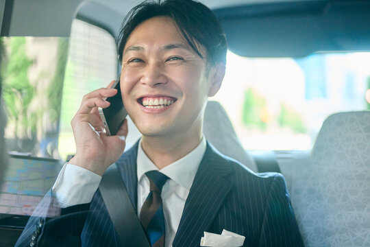 タクシーの車内で笑顔で電話をするビジネスマン