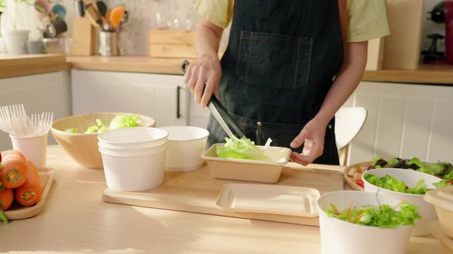 Close up of a woman preparing multiple salad boxes for small food business.