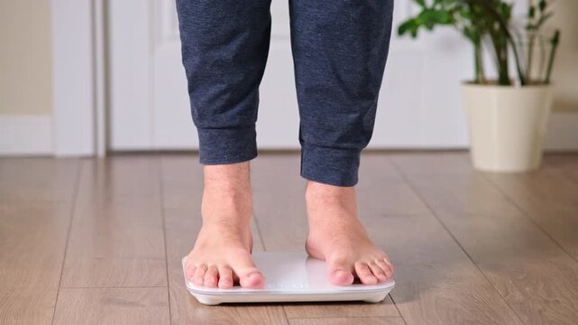Close up of man feet standing on digital bathroom scale on wooden floor at home. Weight control and body mass measurement for diet and healthy lifestyle concept