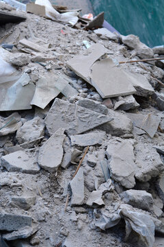 A messy heap of discarded construction waste featuring smashed grey plaster chunks dusty masonry pieces and renovation debris left on the ground.